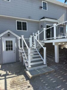 Custom Deck Construction with elegant white railings and stair access to a side door of a modern home.