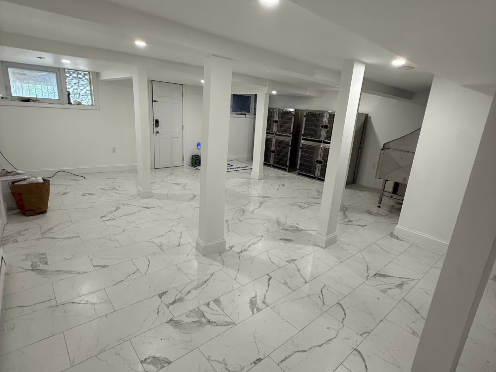 Finished basement with white marble-style tile flooring, white walls, and modern lighting — clean and spacious basement renovation.
